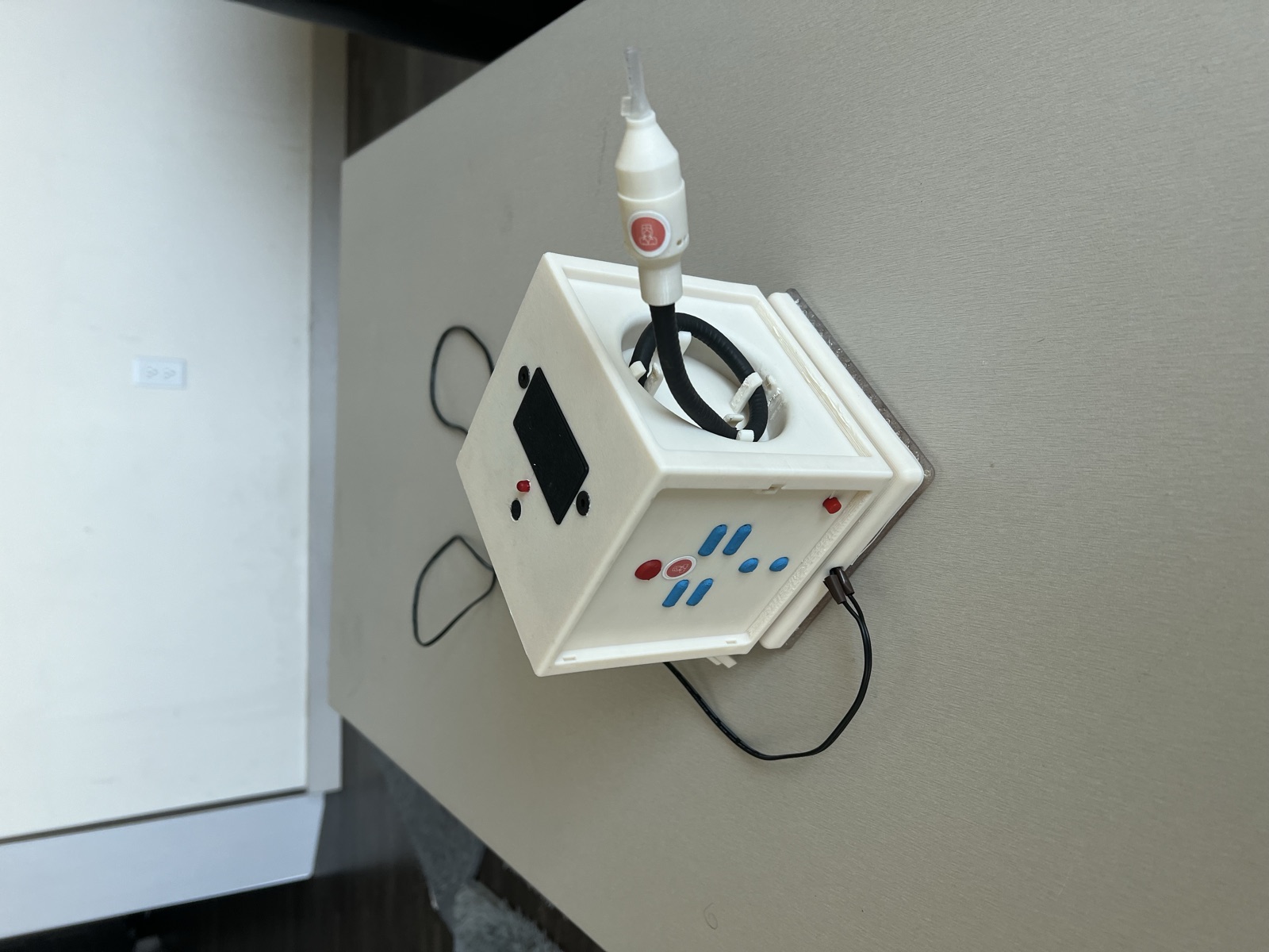 Another side of the prototype showing the remote button pad with raised blue and red buttons, and the breath-call gooseneck coiled in its side storage bay