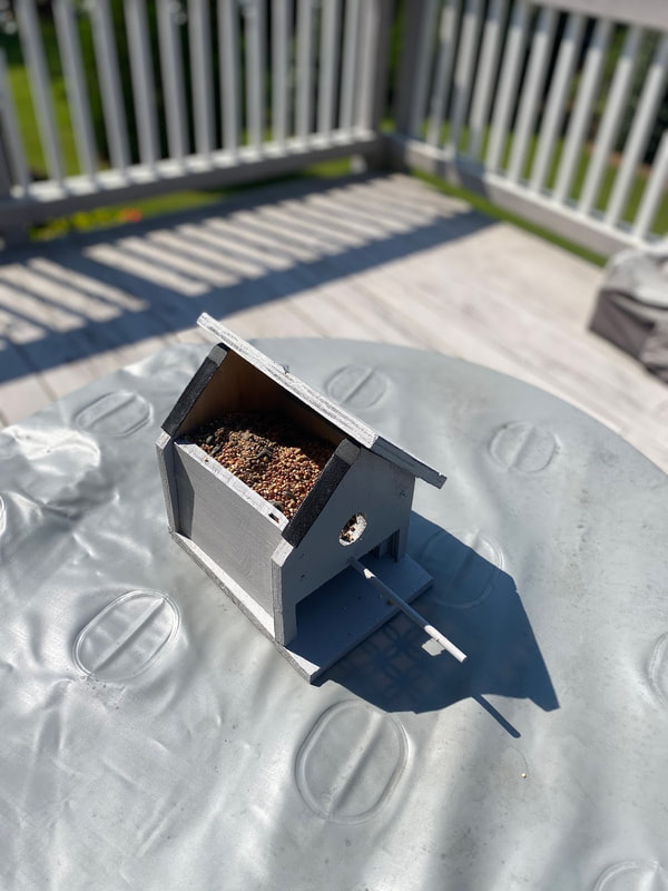 The birdhouse feeder with its roof open, filled with birdseed